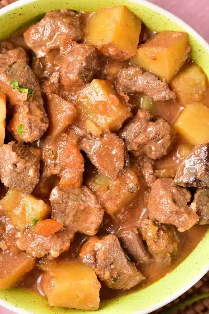 A close-up view of a bowl filled with a hearty beef stew, featuring tender chunks of beef, potato pieces, and a rich brown sauce. The stew appears thick and savory, with visible herbs and vegetables mixed in—reminiscent of a classic Venison Stew Recipe.