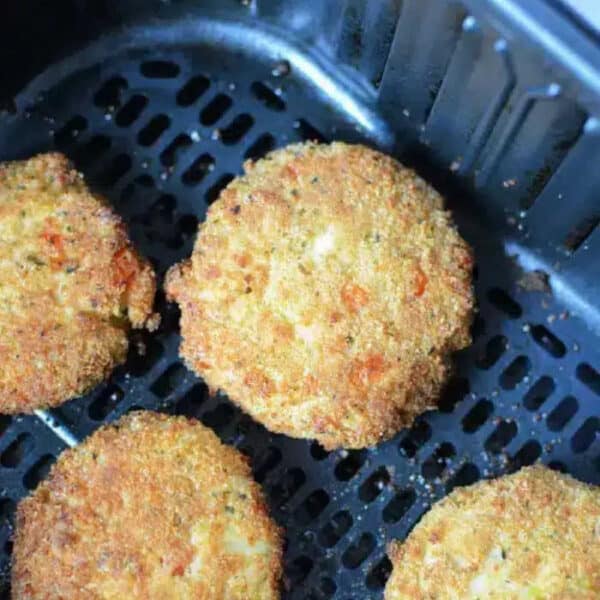 Four golden-brown Air Fryer Crab Cakes rest in the basket, perfectly breaded and ready to be served.