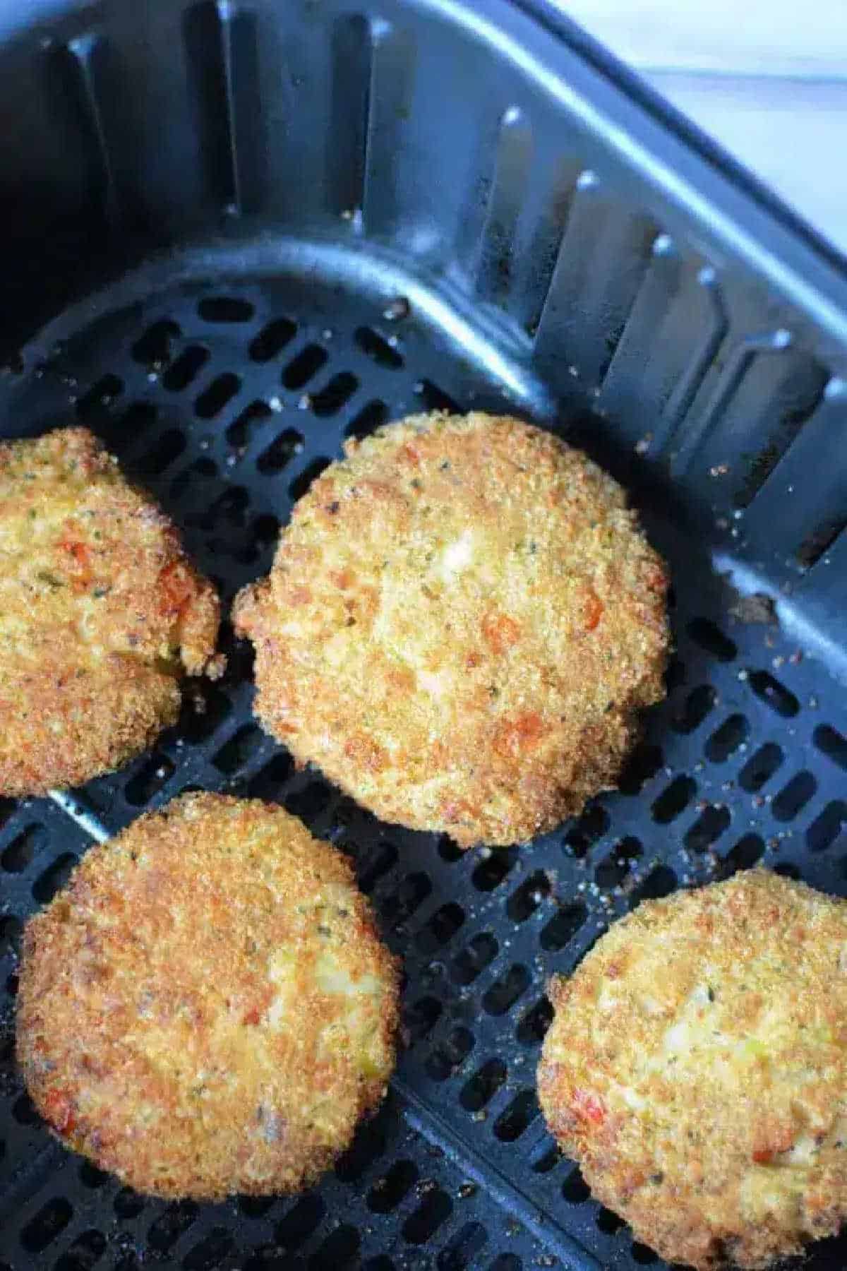Four golden-brown Air Fryer Crab Cakes rest in the basket, perfectly breaded and ready to be served.