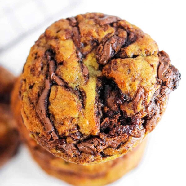 Close-up of a stack of Banana Nutella Muffins with visible chunks of chocolate on a white background, tempting enough to rival the allure of freshly baked Banana Nutella Muffins.