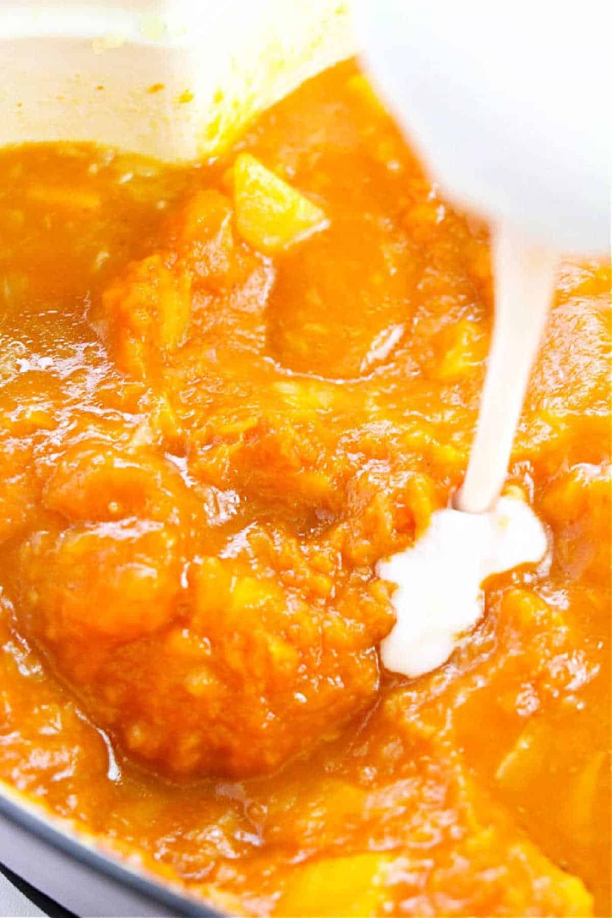Coconut milk is being poured into a pot of thick pumpkin soup, creating a creamy Pumpkin Soup with Canned Pumpkin.