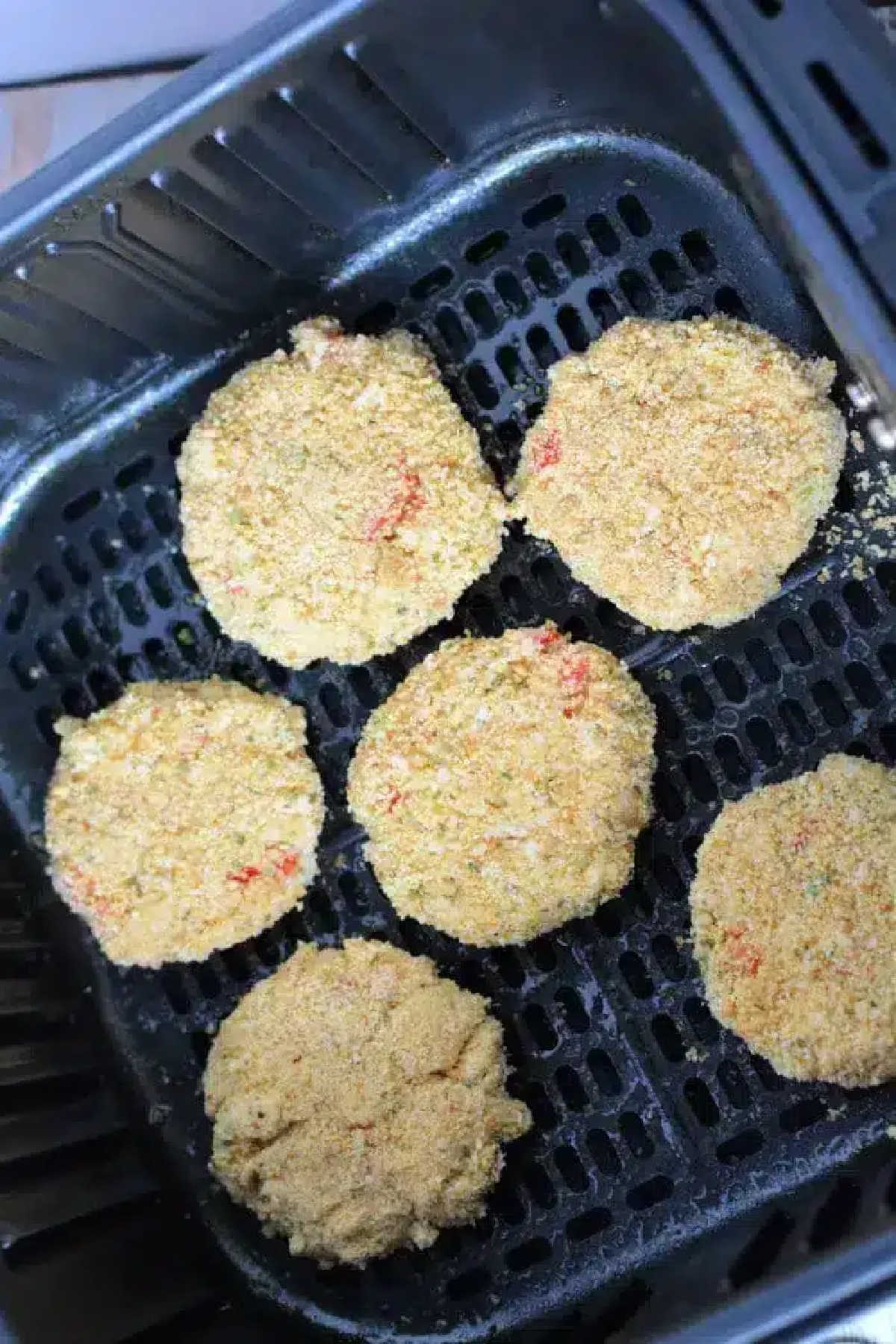 Five breaded Air Fryer Crab Cakes arranged in an air fryer basket, ready to be cooked.