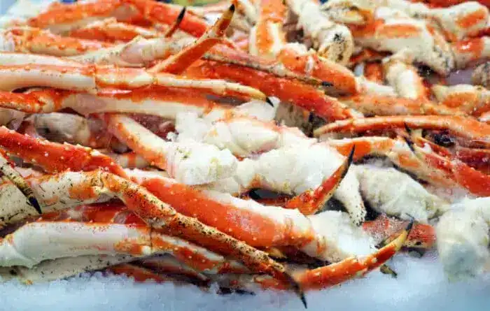 A pile of fresh crab legs is displayed on crushed ice at a seafood market. 