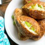 Ninja Foodi baked potatoes split open and topped with chopped green onions on a white plate.