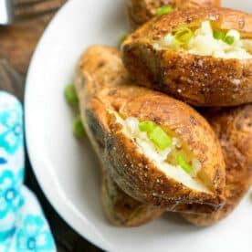 Ninja Foodi baked potatoes split open and topped with chopped green onions on a white plate.