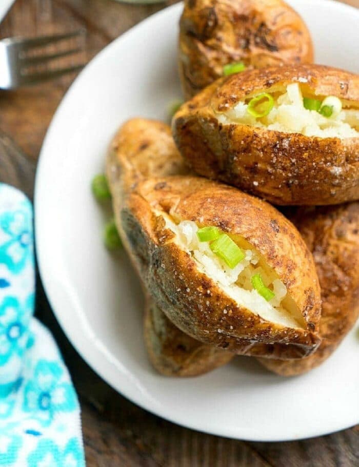 Ninja Foodi baked potatoes split open and topped with chopped green onions on a white plate.