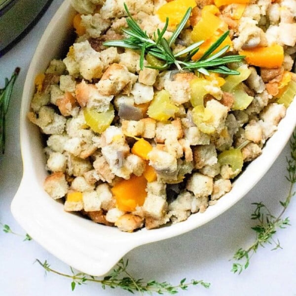 A white dish filled with delicious instant pot stuffing, topped with herbs and diced vegetables like celery and squash.