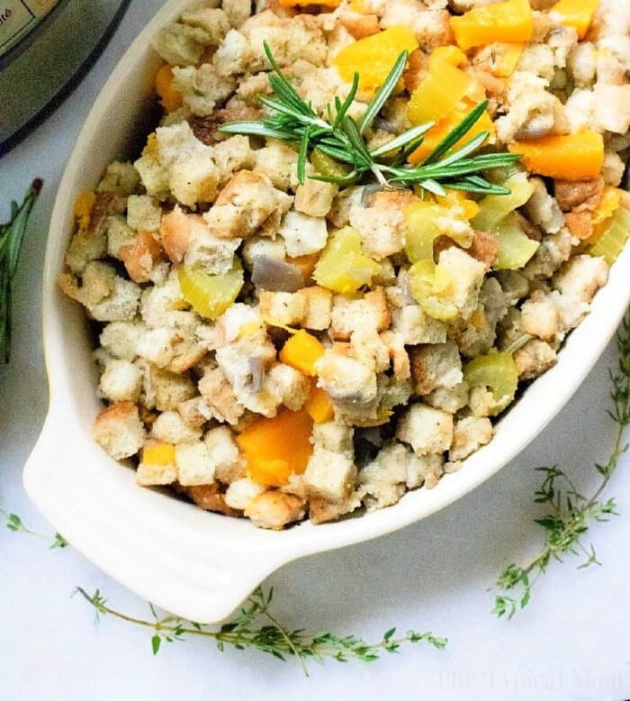 A white dish filled with delicious instant pot stuffing, topped with herbs and diced vegetables like celery and squash.