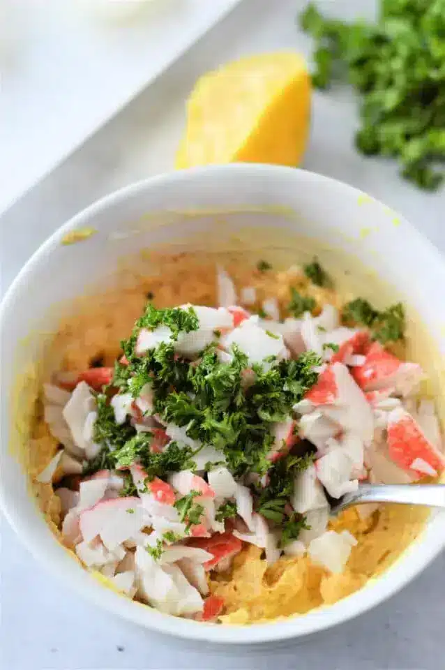 A bowl of mixed ingredients, including chopped imitation crab meat and a sprinkle of chopped parsley on top. 