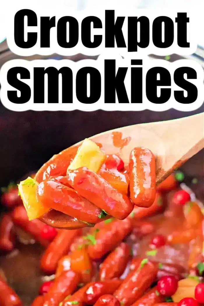 A wooden spoon holds cocktail sausages, pineapple chunks, and cherries above a crockpot. The text "Crockpot Little Smokies Recipe" is prominently displayed at the top, inviting you to try this delightful dish.