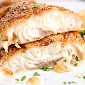 Close-up of crispy air fryer catfish, coated in golden breadcrumbs, topped with fresh herbs, and served with vibrant lemon slices.