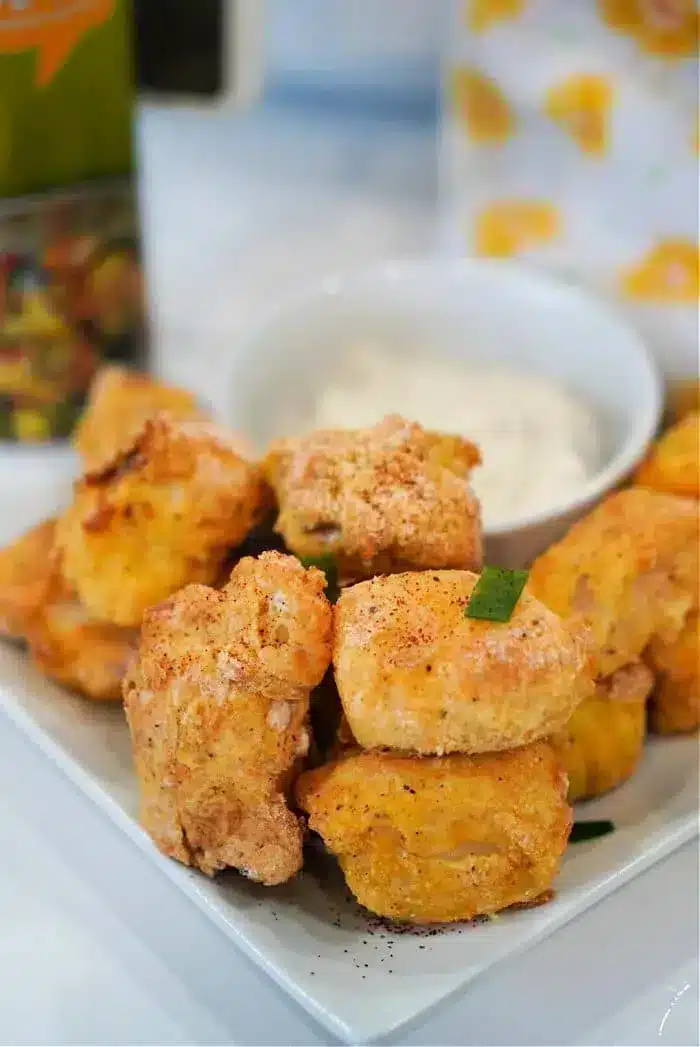 A white plate filled with pieces of cooked, breaded chicken sits next to a small bowl of white dipping sauce. The chicken pieces are golden brown and garnished with chopped green onions, reminiscent of how air fryer fish sticks are served for that perfect crispy texture.