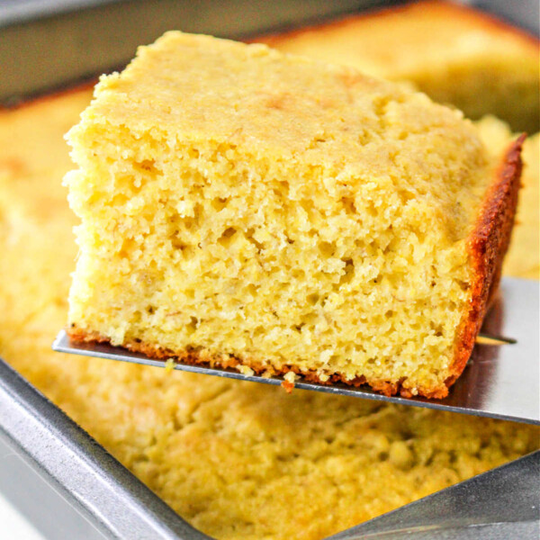 A slice of golden banana cornbread being lifted from a baking pan.