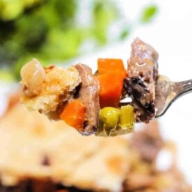 A close-up of a fork holding a bite of meat, carrots, peas, and pie crust from a delicious Leftover Steak Pot Pie.