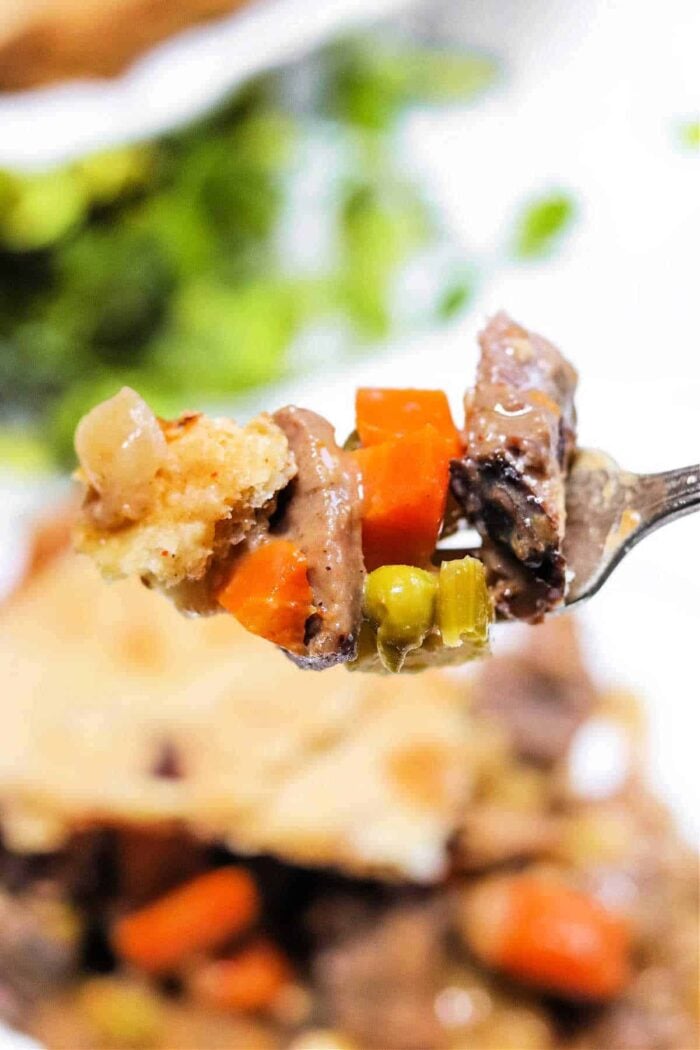 A close-up of a fork holding a bite of meat, carrots, peas, and pie crust from a delicious Leftover Steak Pot Pie.