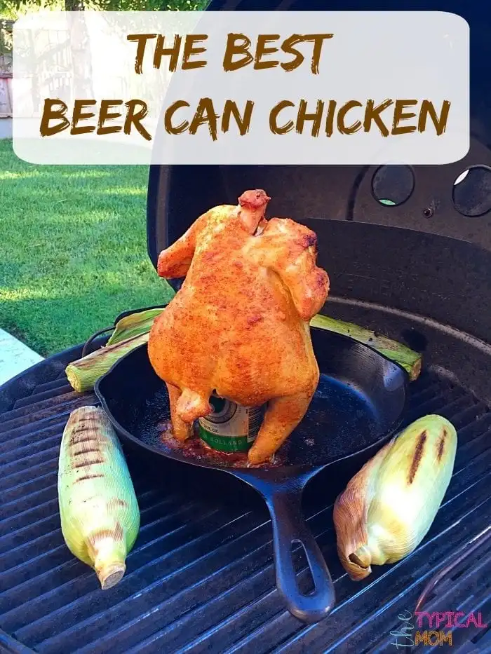 A whole roasted chicken sits atop a beer can on a charcoal grill, nestled in a cast iron skillet amid partially husked corn. The scene is set against a green lawn backdrop with text at the top proclaiming "THE BEST BEER CAN CHICKEN.