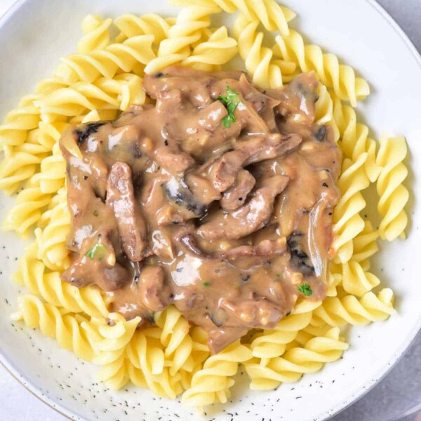 A plate of spiral pasta topped with creamy venison stroganoff, garnished with a sprig of parsley.