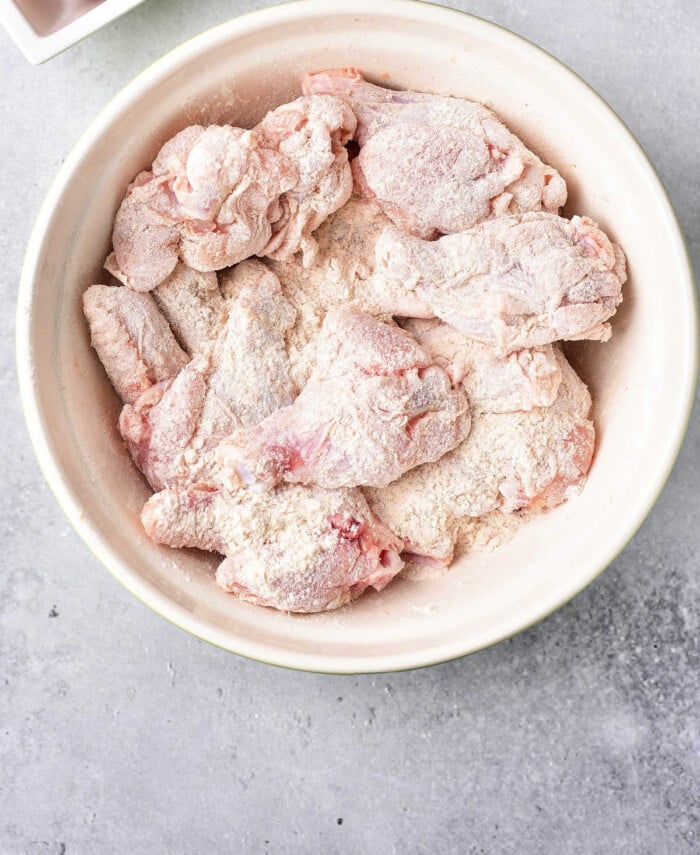 Raw chicken wings coated in baking powder sit in a white bowl on a gray surface, the perfect start for learning how to bake crispy chicken wings.