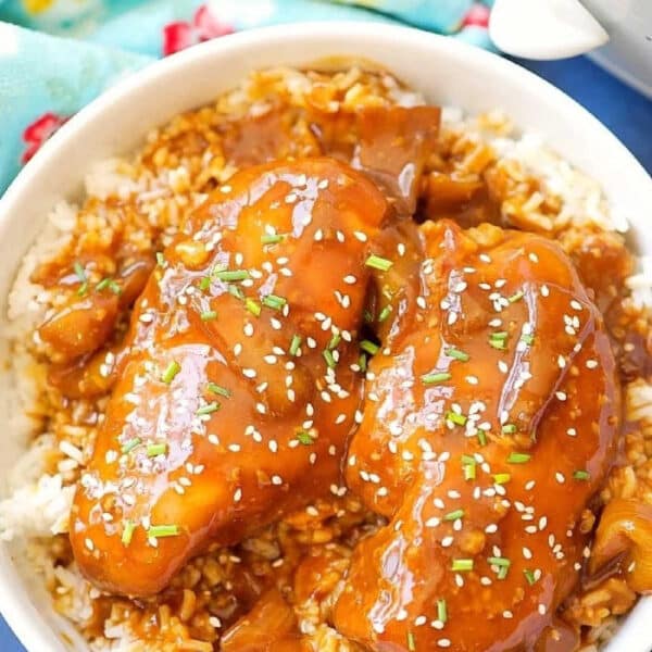 Bowl of rice topped with crockpot teriyaki chicken, chopped herbs, sesame seeds, and a savory brown sauce.