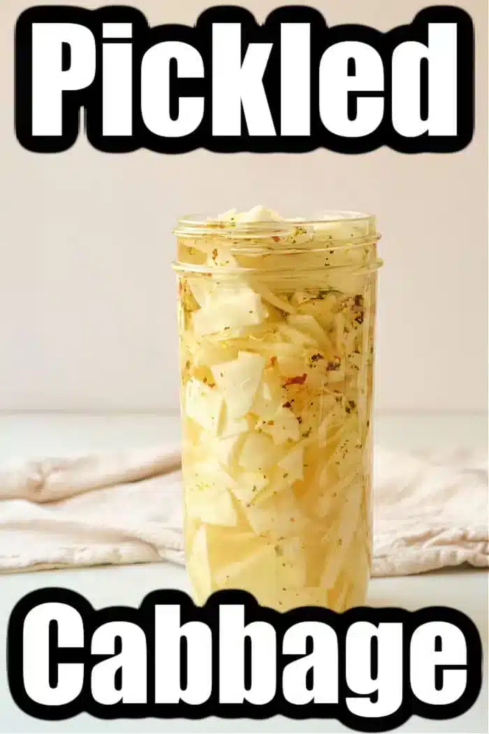 A glass jar of quick pickled cabbage sits on a light surface. Packed with sliced cabbage in a yellowish brine, the words "Quick Pickled Cabbage" are prominently displayed above and below. A cloth is in the background, adding a touch of rustic charm to the scene.