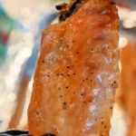 A close-up of a baked turkey wing, crispy and golden, held by someone in a black glove against a softly blurred background. The text "How to Bake Crispy Turkey Wings" is prominently displayed at the top of the image.