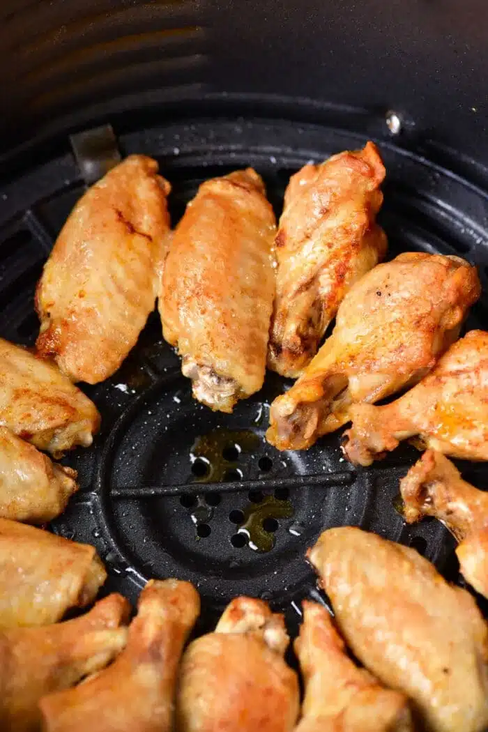 Golden-brown chicken wings, reminiscent of their tender boiled counterparts, are arranged in a circle inside an air fryer basket.