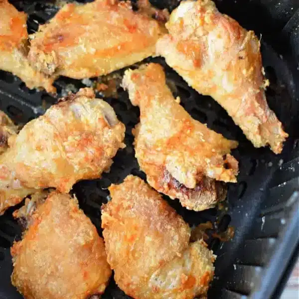 Eight pieces of crispy, golden-brown chicken wings are shown inside a black air fryer basket. The wings have a slightly uneven, textured surface, indicating they are well-cooked and well-seasoned. Thanks to the addition of baking powder, these air fryer chicken wings achieve their delightful crunch.