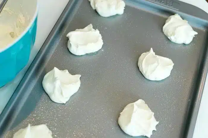 Dollops of white cream, almost as soft and airy as angel food cake, rest on a baking sheet next to a blue bowl.