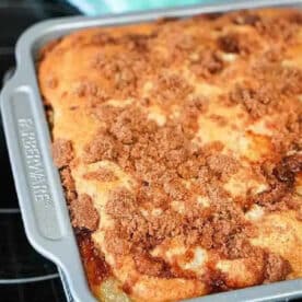 A cinnamon crumb coffee cake, inspired by a 3 ingredient dump cake, sits in a baking pan, fresh out of the oven and cooling on a wire rack.