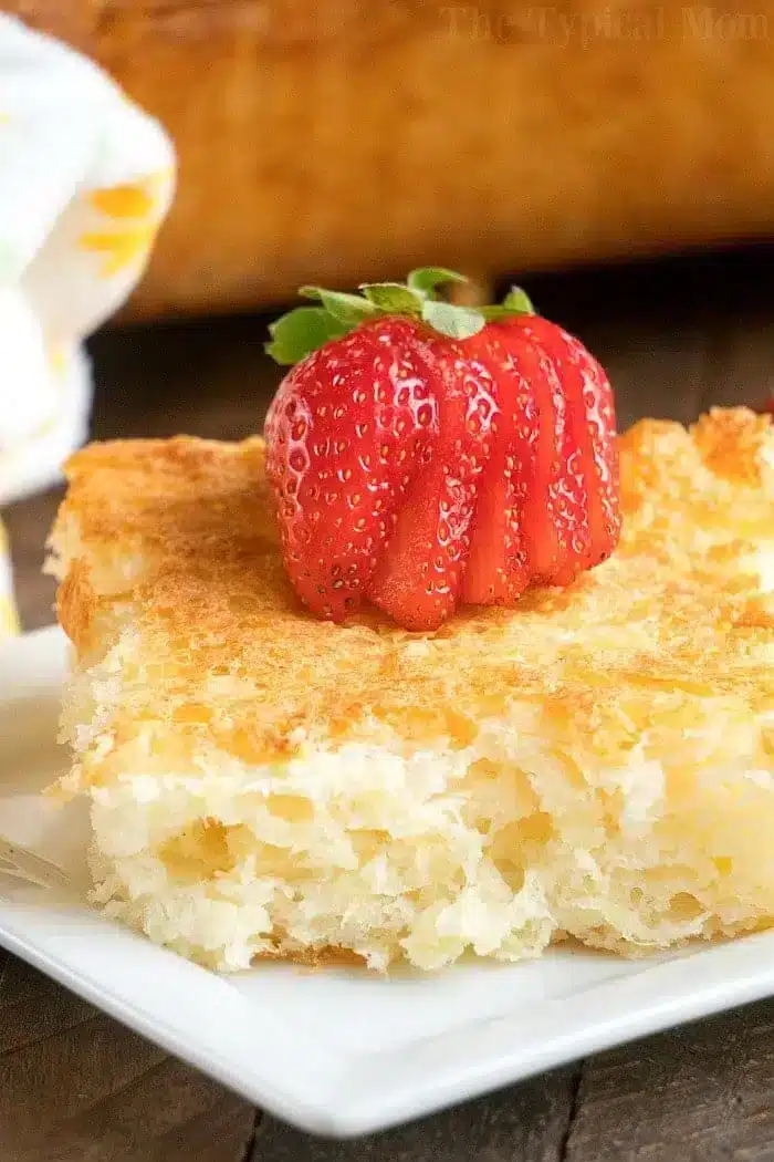 A close-up of a piece of golden-brown bread pudding on a white plate, topped with a strawberry sliced fan-like. 