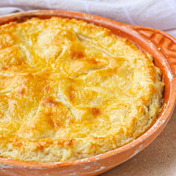 Golden-brown pie with a delectable sourdough pie crust in a round, orange baking dish on a light surface, accented by a checkered cloth in the background.