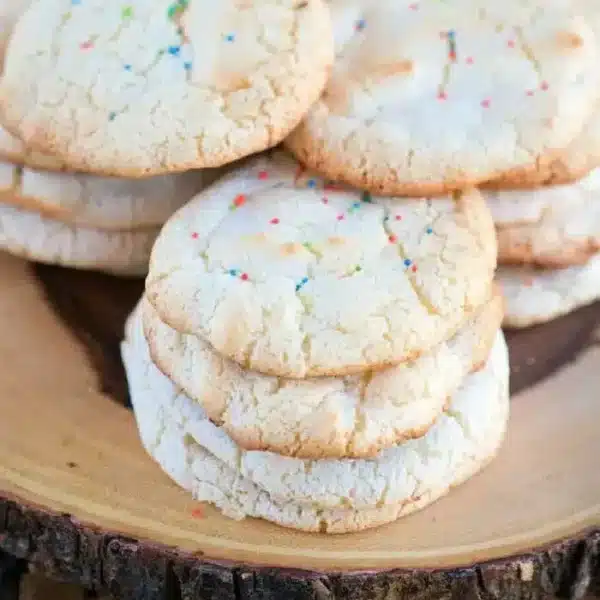 A stack of six sugar cookies made from angel food cake mix with rainbow sprinkles sits on a wooden platter.