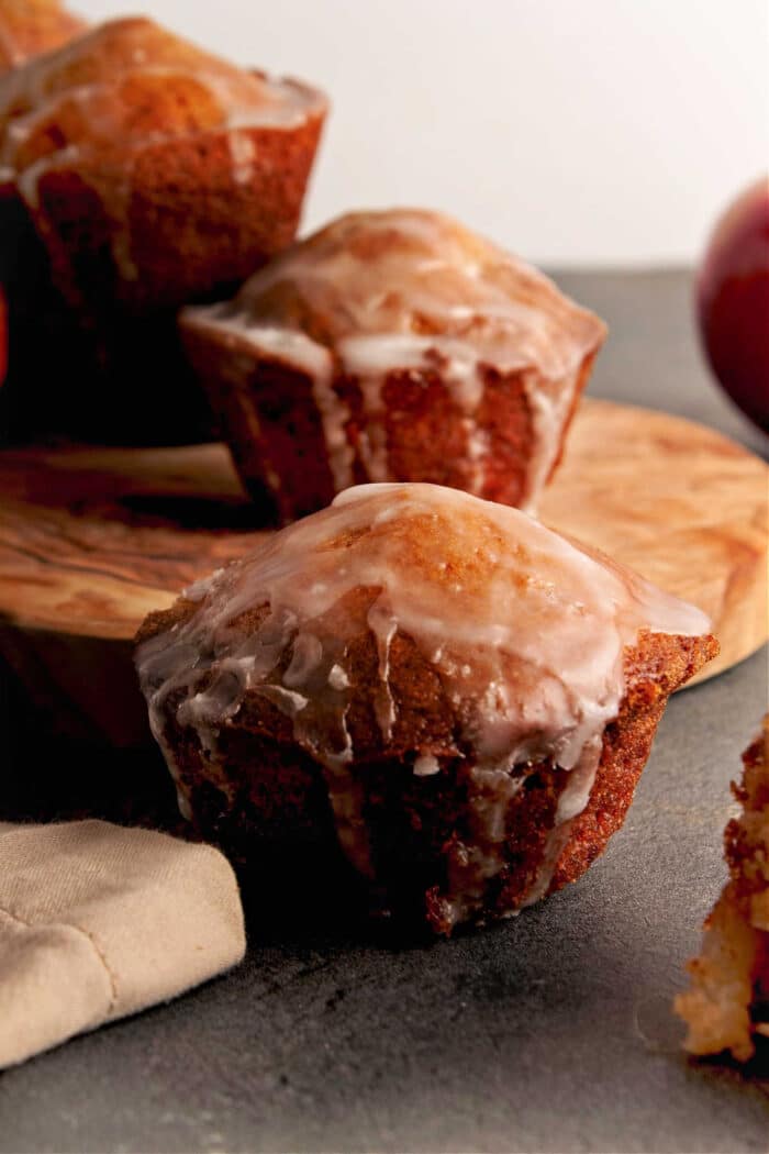 Close-up of glazed apple fritter muffins on a wooden board and gray surface.