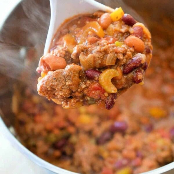 A white ladle holds a hearty blend reminiscent of an easy Bloody Mary chili recipe, featuring kidney beans, ground meat, and diced vegetables over a steaming pot filled with the same savory mixture.