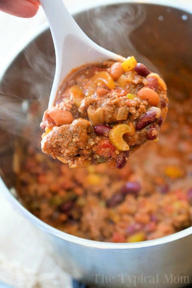 A white ladle holds a hearty blend reminiscent of an easy Bloody Mary chili recipe, featuring kidney beans, ground meat, and diced vegetables over a steaming pot filled with the same savory mixture.