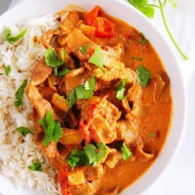 A bowl of rice and creamy curry with vegetables, featuring tender instant pot butter beef and garnished with fresh cilantro, on a white cloth.