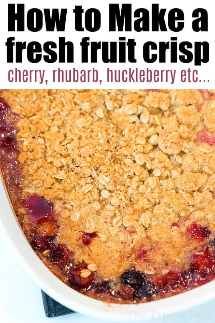 Golden brown cherry crisp recipe with oats on top and visible cherry, rhubarb, and huckleberry filling in a white dish.