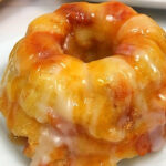 Mini bundt cake topped with a thick, glossy caramel and white icing, reminiscent of a classic caramel apple bread pudding, served on a white plate.