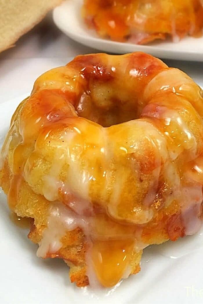 Mini bundt cake topped with a thick, glossy caramel and white icing, reminiscent of a classic caramel apple bread pudding, served on a white plate.