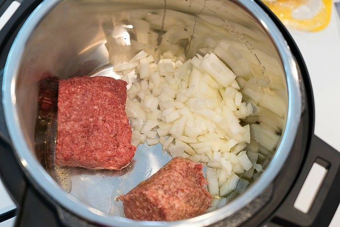 Ground beef and chopped onions in an electric pressure cooker, ready to whip up a flavorful mild chili recipe.