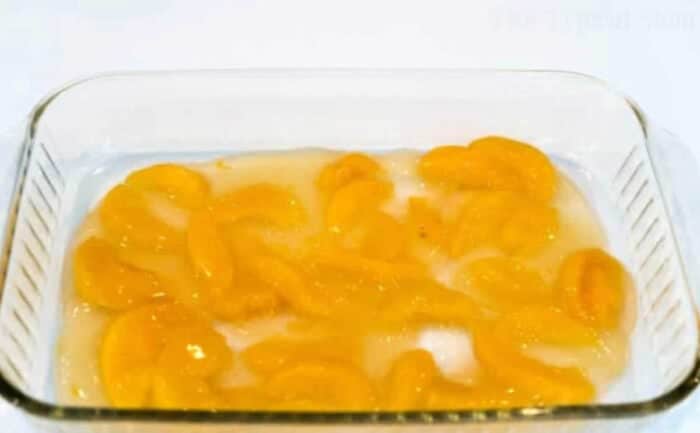 Glass dish with canned peach slices in syrup on a white surface, perfect for making an effortless dump peach cobbler.