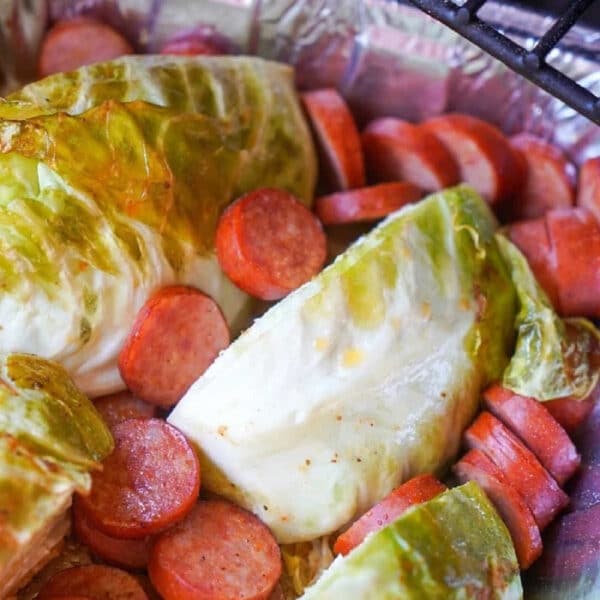 Smoked sausage and cabbage wedges are arranged in a foil pan on a grill, ready for a flavorful meal.
