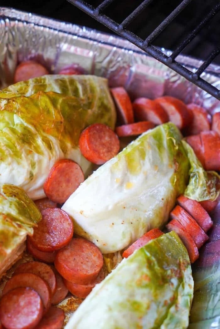 Smoked sausage and cabbage wedges are arranged in a foil pan on a grill, ready for a flavorful meal.