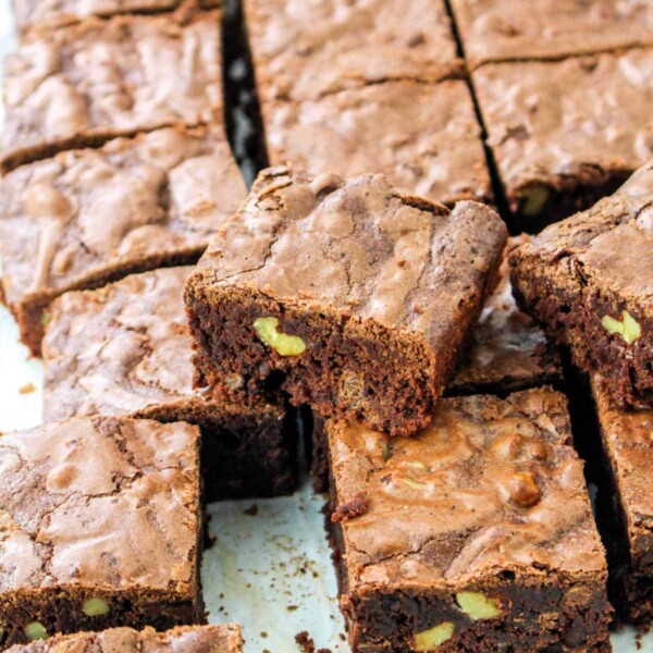 The decadent 100 Hour Brownies, rich with nuts and expertly cut into squares, are perfectly stacked on a pristine white surface.