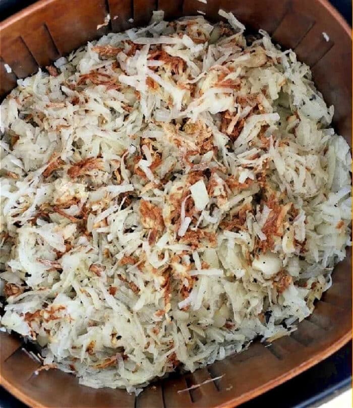 Air fryer hash browns, shredded and golden brown in spots, cooking to crispy perfection in an air fryer basket.
