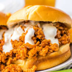 Close-up of slow cooker ground chicken sloppy joe sandwich with creamy sauce on a bun, next to a few celery sticks.