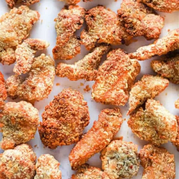 Crispy, golden-brown air fryer popcorn chicken pieces arranged on a white surface.