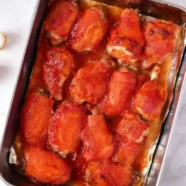 Chicken wings covered in a red sauce, possibly marinara or barbecue sauce, sits on a light-colored countertop to bake in oven.