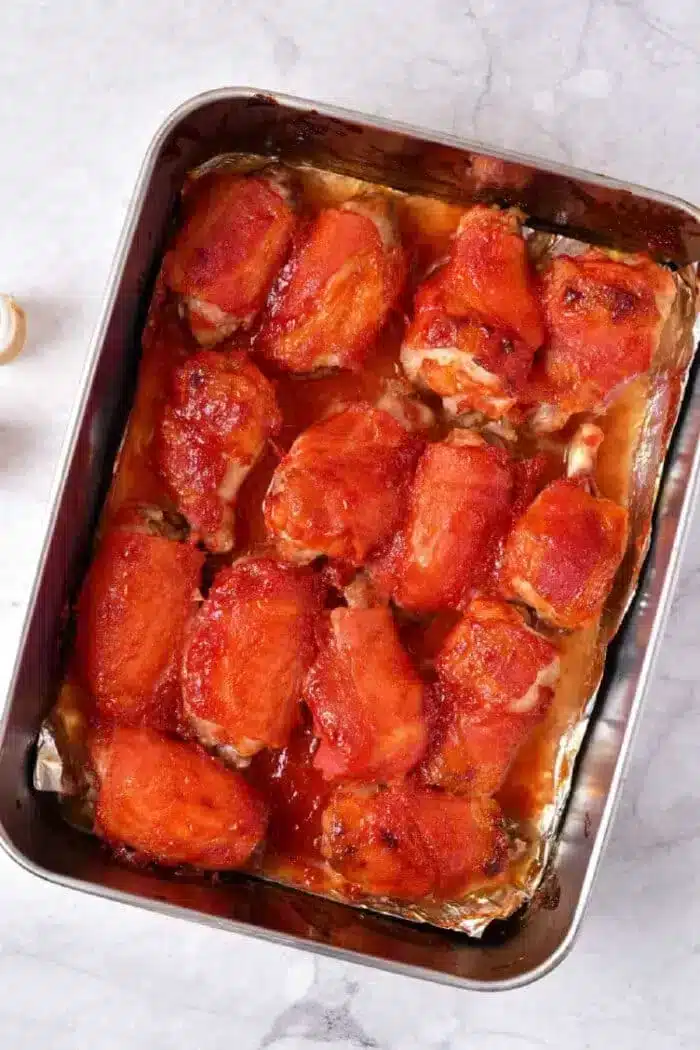 A metal baking dish filled with several pieces of chicken covered in a red sauce.