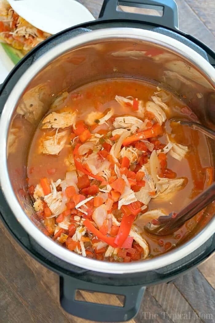 Instant Pot salsa chicken, shredded with diced vegetables and broth, is served warm on a wooden table.